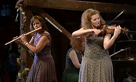 A woman plays the flute on the left of the stage and to the right a second woman plays the violin.