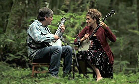 Fleck and Washburn play their banjos in a lush forest.