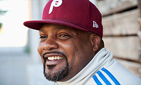 Harris smiles on the street wearing a track jacket and Phillies baseball cap.