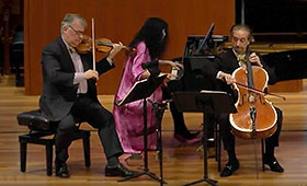 A violinist, pianist, and cellist perform on stage.