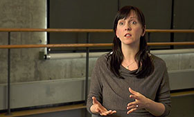 Choreographer Jessica Lang, sitting in a sparse dance studio, gestures while explaining her production of Thousand Yard Stare.