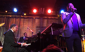 Jazz musician Ramsey Lewis, sitting at his piano, accompanies vocalist Philips Bailey during a live performance.