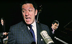 John Pizzarelli, wearing a suit and tie, sings into a microphone.