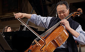 Yo-Yo Ma plays the cello while Kathryn Stott plays the piano behind him.