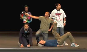 Two men crouch on the ground next to a third on his back while two students stand behind them on stage.