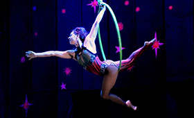 An acrobat stretches through a hoop thathangs from the ceiling
