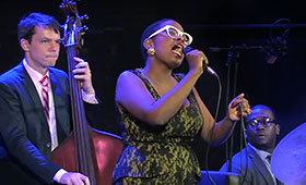 Salvant sings into the microphone as a bassist and drummer perform beside her.